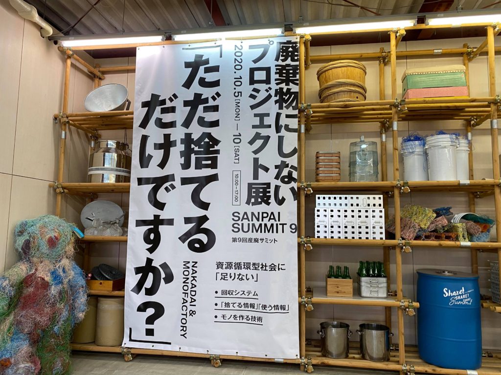 第9回産廃サミット会場の懸垂幕。「ただ捨てるだけですか？」という大きな文字と「廃棄物にしないプロジェクト展」などの情報が記載されています。